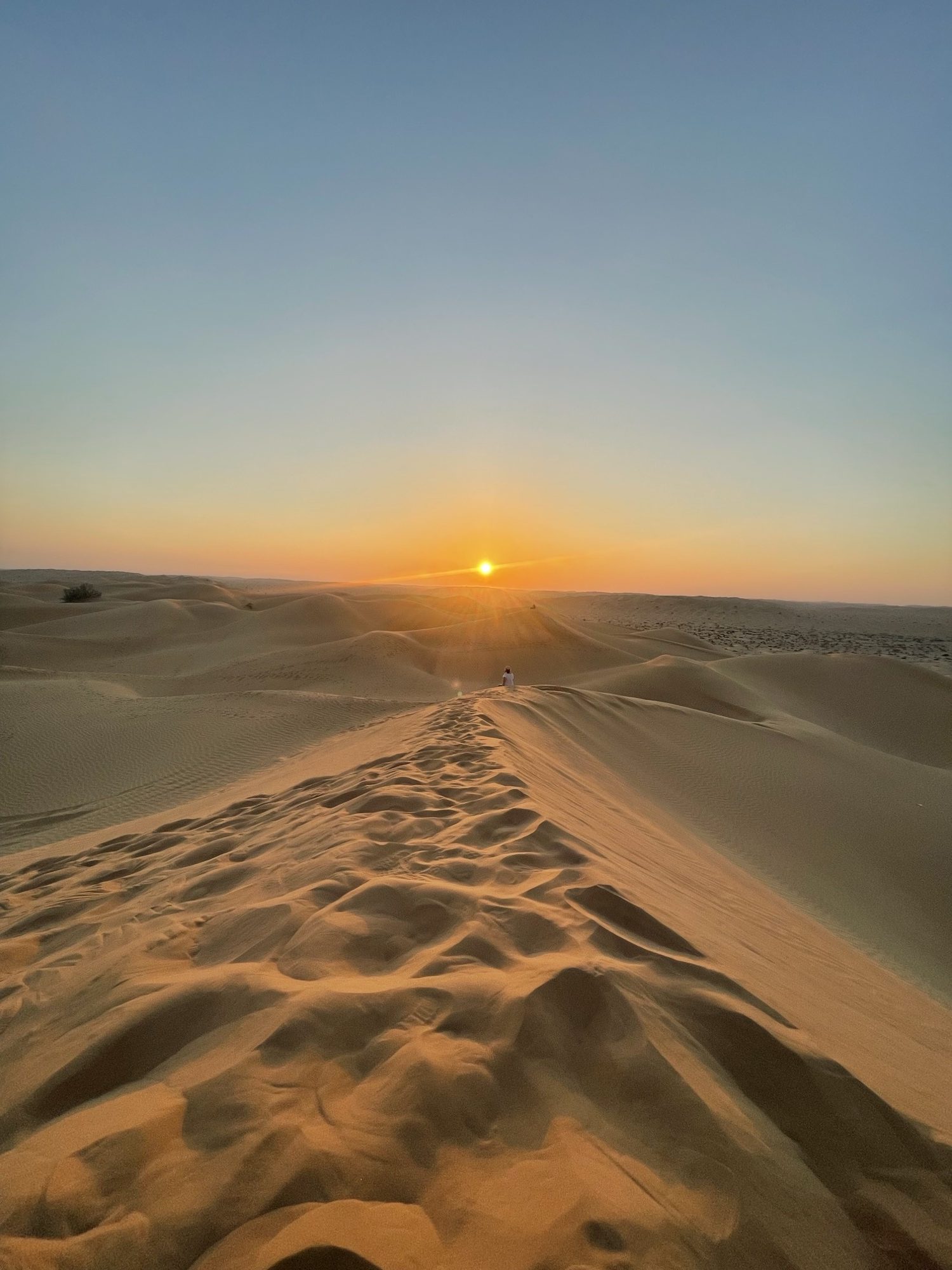 Voetsporen over de duinrug, de zon laag boven de horizon