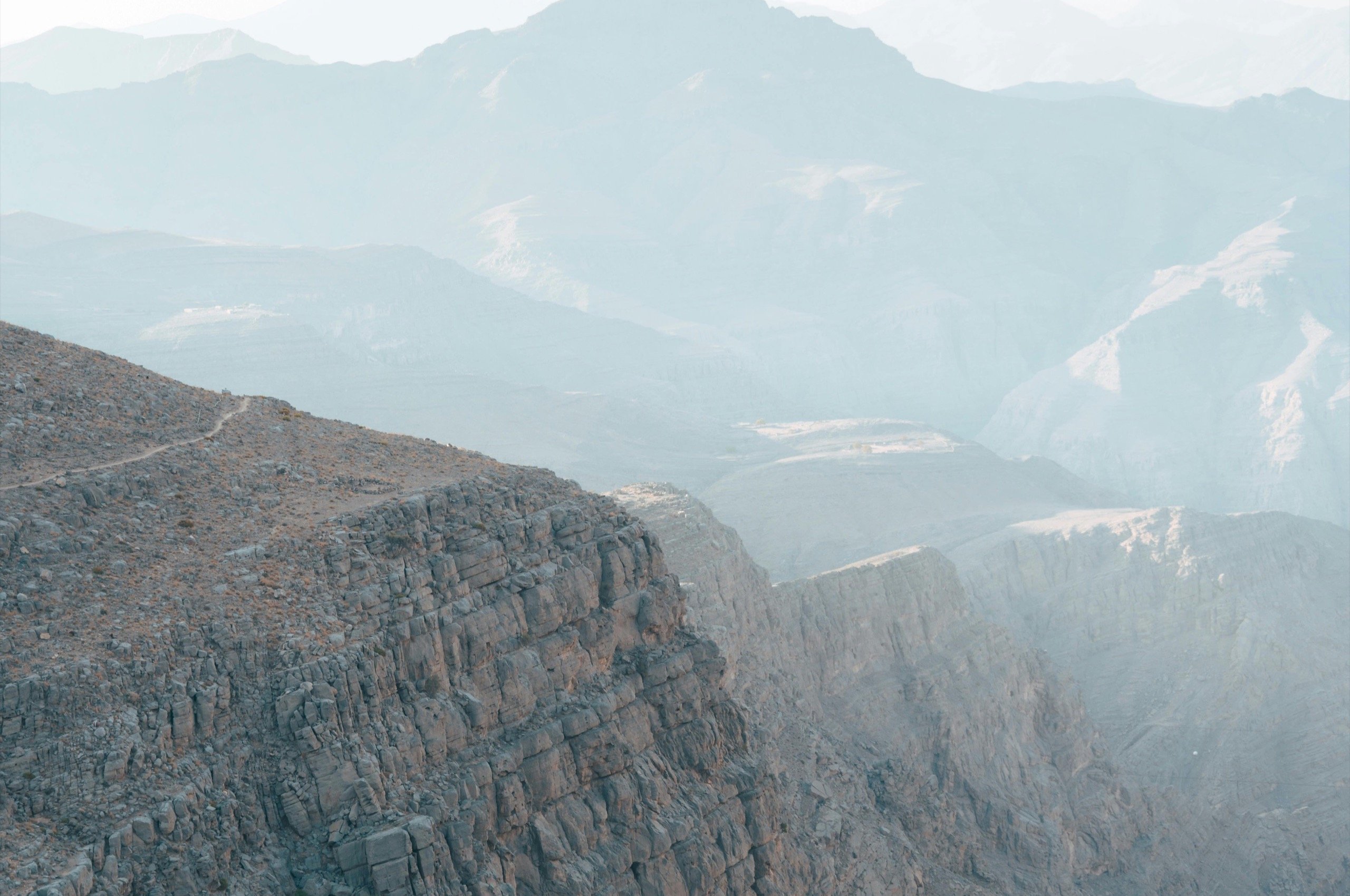 De kloofrand van Jebel Shams, met de toppen van het Hajar-gebergte in de ochtendnevel